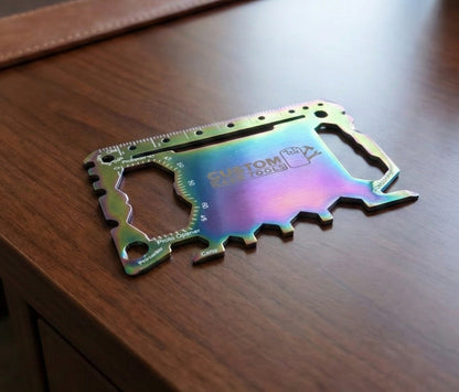 An iridescent rainbow-colored metal multi-tool card, branded 'CUSTOM CAR TOOLS', resting on a dark wood tabletop.