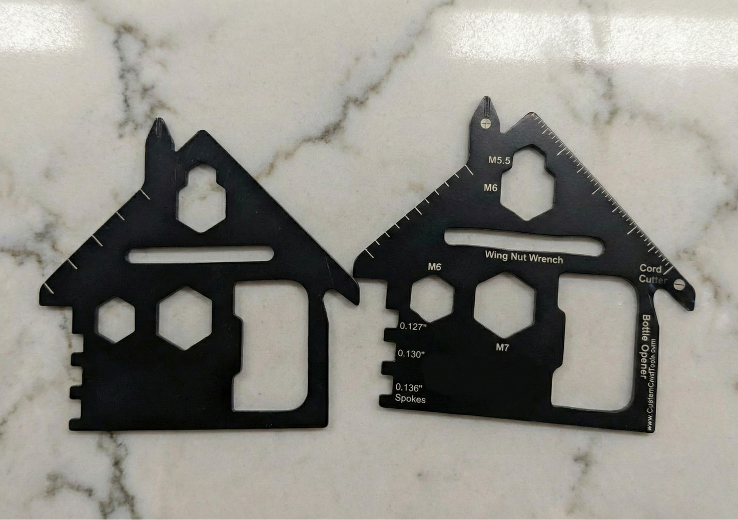 Two black multi-tool cards shaped like houses on a marble surface