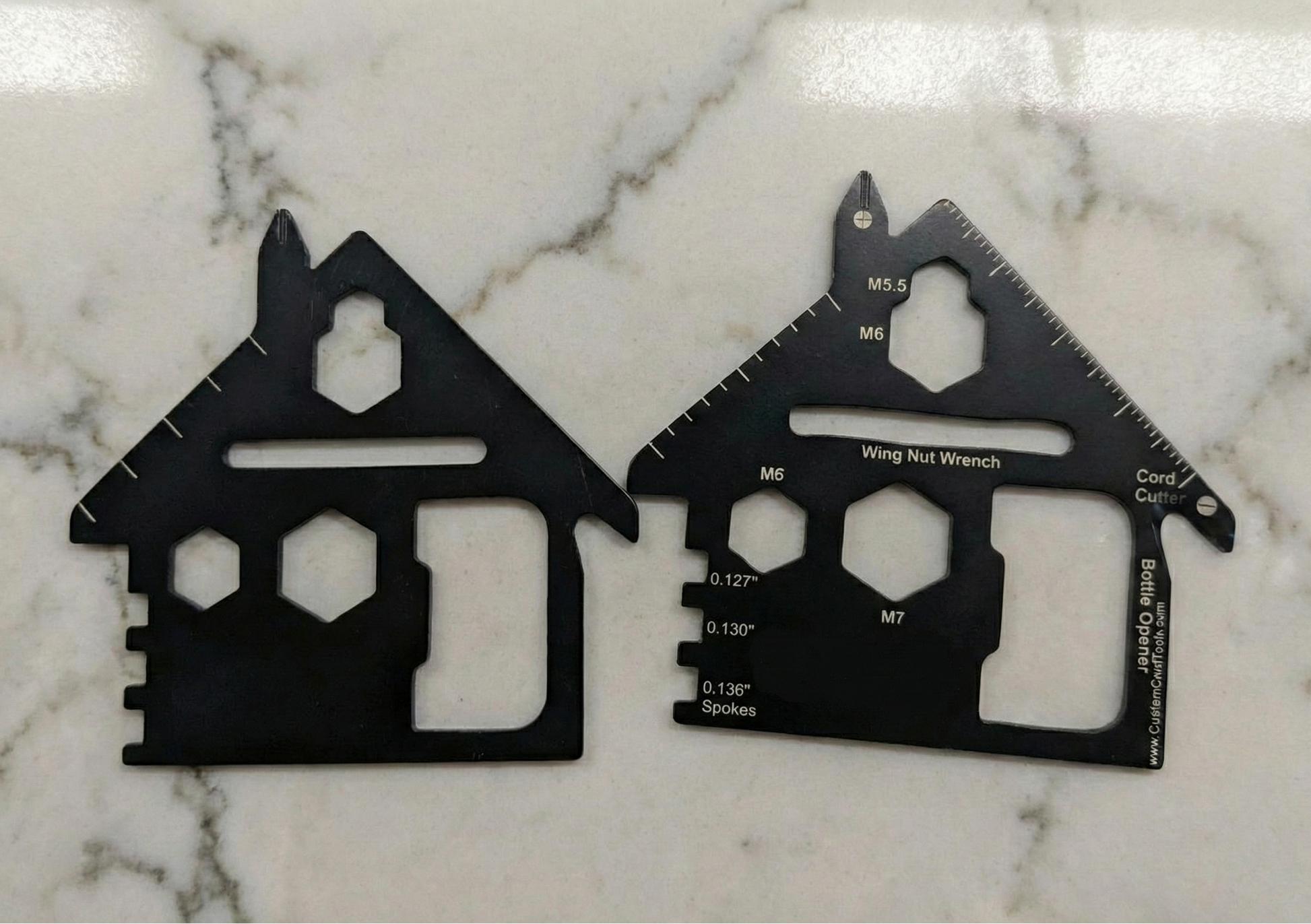 Two black multi-tool cards shaped like houses on a marble surface