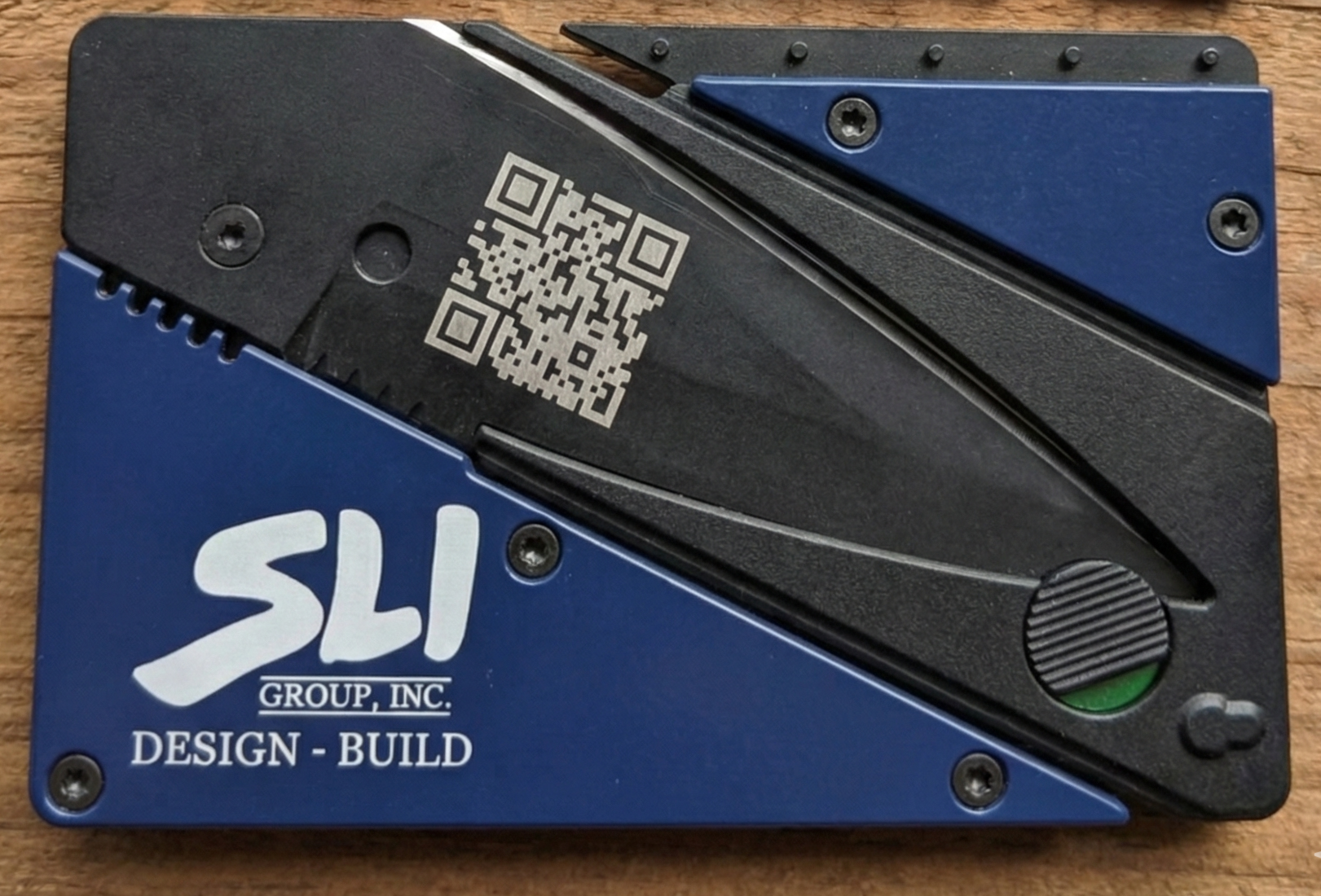 folding card knife with QR code and SLI Group, Inc. branding on a wooden surface