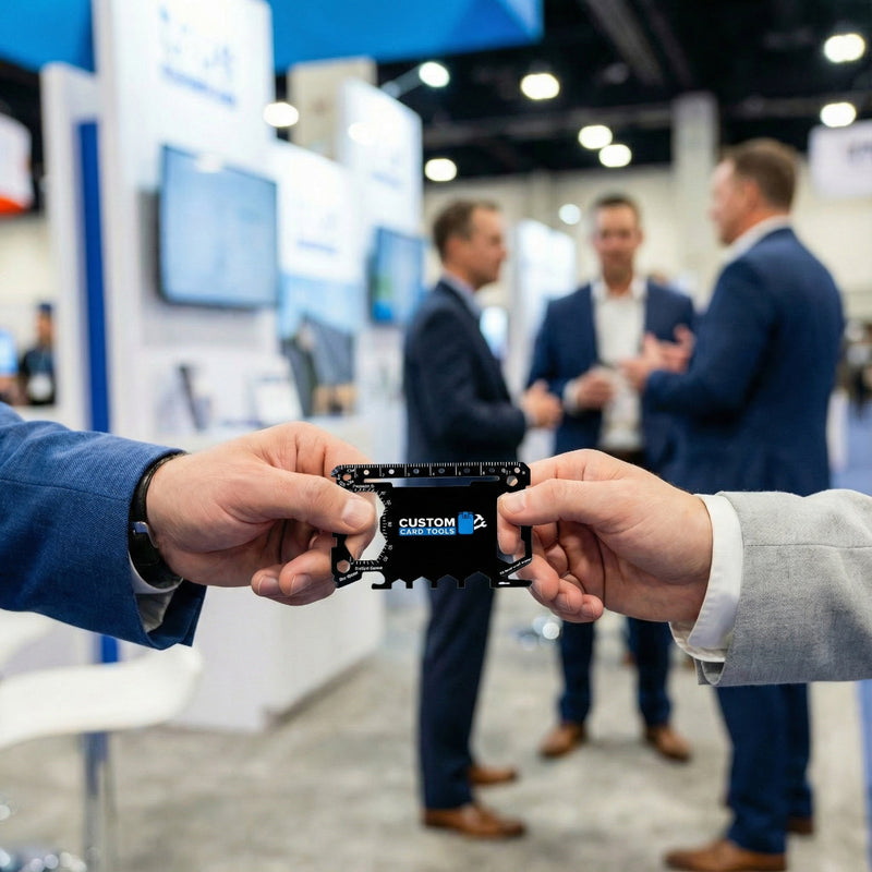 Two hands exchanging a metal business card at a trade show with blurred people in the background