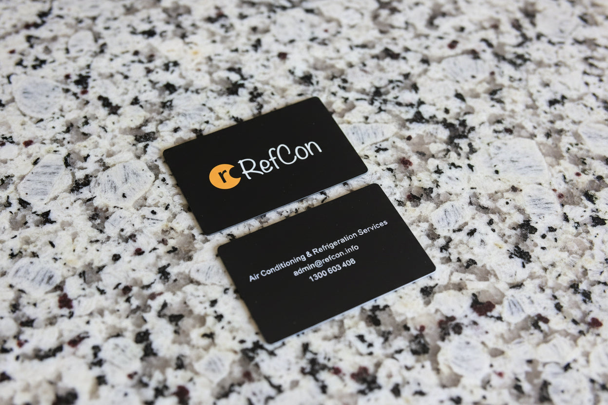 Two metal business cards with RefCon logo and contact information on a granite surface