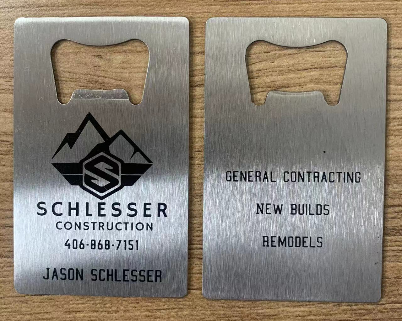 Two metal bottle openers with Schlesser Construction branding on a wooden surface.