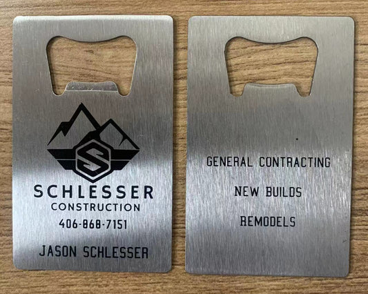 Two metal bottle openers with Schlesser Construction branding on a wooden surface.